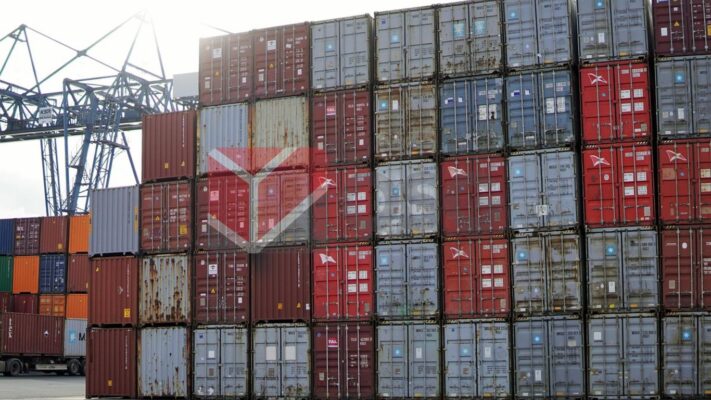 Stacked shipping containers in a port area under bright skies.