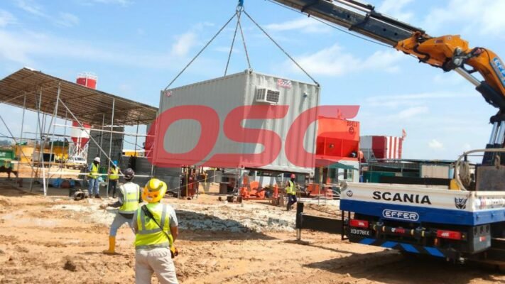 Crane lifting container at construction site with workers.