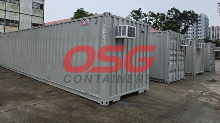Several grey shipping containers with air conditioning units are lined up.