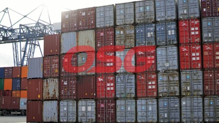 Stack of shipping containers at a port with a crane.