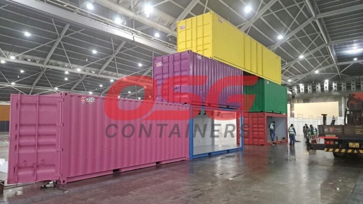 Stacked colorful shipping containers inside a large warehouse with workers.